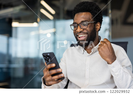 Successful man close up inside office celebrating victory and successful achievement results, businessman holding phone in hands, received notification of triumph. Successful man close up inside office celebrating victory and successful achievement results, businessman holding phone in hands, received notification of triumph. 122029932