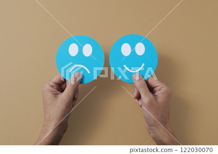 holding a sad face and a happy face in his hands 122030070