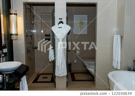 Primary bathroom interior with free standing bath tub floating cabinets walk in shower windows with black frames spa robe hanging on a hanger grey slate flooring Primary bathroom interior with free standing bath tub floating cabinets walk in shower windows with black frames spa robe hanging on a hanger grey slate flooring 122030639