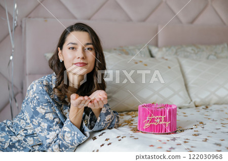 Young woman blowing golden confetti on her birthday cake 122030968