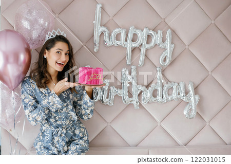 Woman celebrating birthday holding pink cake with balloons and happy birthday sign 122031015