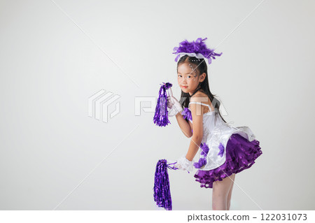 Portrait of a cheerful cheerleader girl in a purple and white outfit, holding purple pom-poms. Smiling brightly in a studio shot against white background. Energetic and festive vibes. cheerleader kid 122031073