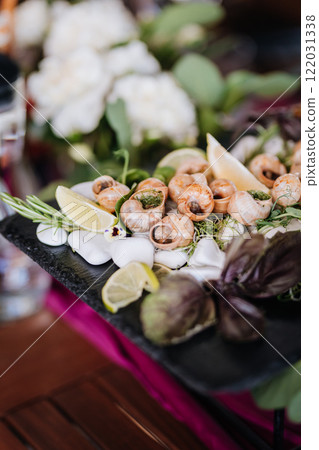 Gourmet escargot platter with fresh herbs and lemon, elegantly presented on a slate serving board Gourmet escargot platter with fresh herbs and lemon, elegantly presented on a slate serving board 122031338