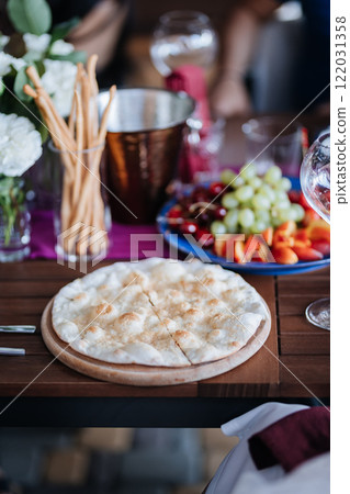 Delicious flatbread served alongside fresh fruit and breadsticks on a beautifully set dining table Delicious flatbread served alongside fresh fruit and breadsticks on a beautifully set dining table 122031358