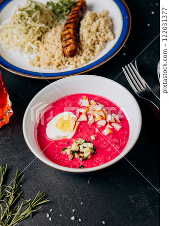 Colorful business lunch with grilled sausage, couscous, cabbage salad, and beet soup with boiled egg Colorful business lunch with grilled sausage, couscous, cabbage salad, and beet soup with boiled egg 122031377