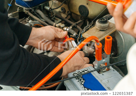 two men are repairing a car on the road. replacing the fuel filter under the hood of the car 122031387