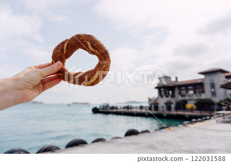 Turkish simit in hand with bay in background. Hot sesame bun with sea in background. 122031588