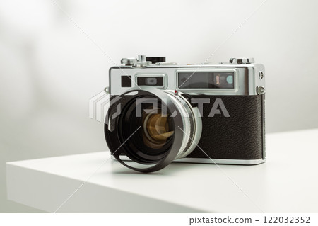 A vintage film camera sits elegantly on a white surface, showcasing its timeless design. A vintage film camera sits elegantly on a white surface, showcasing its timeless design. 122032352