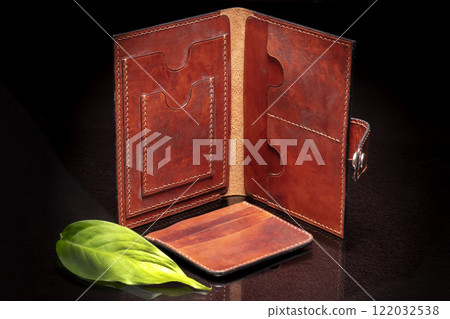 Leather brown open purse and green leaf on a dark background. 122032538