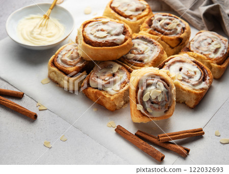 Freshly baked cinnamon rolls topped with cream cheese frosting and almond slivers 122032693