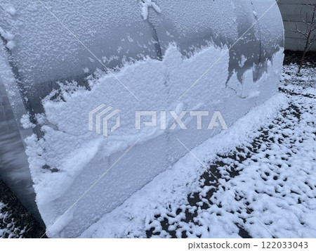 Greenhouse covered with snow in a rural garden 122033043
