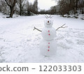 A snowman stands on a snowy area near a frozen river surrounded by trees. Concept of winter fun. 122033303