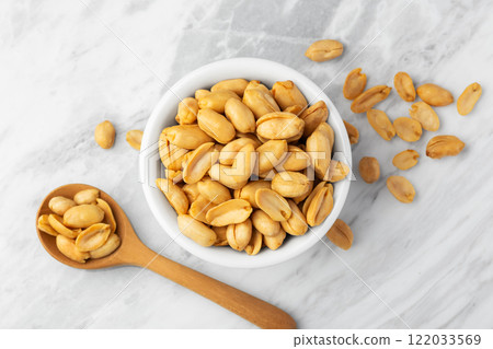Roasted peanuts in white bowl with wooden spoon on marble table 122033569