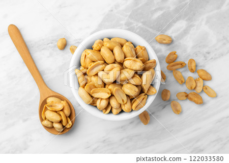 Roasted peanuts in white bowl with wooden spoon on marble table 122033580