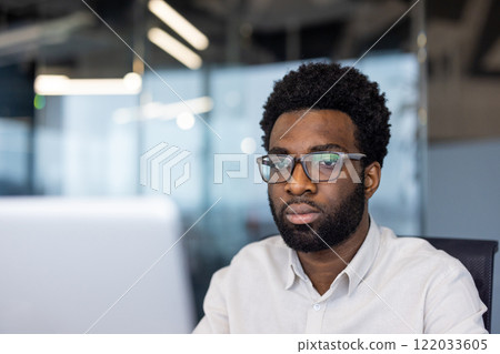 Serious businessman close up working with laptop inside office. Man in shirt reading online report, watching video course, online conference. 122033605