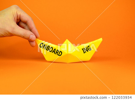 Onboarding success symbol. Concept word Onboarding on beautiful yellow paper boat. Beautiful orange background. Businessman hand. Business onboarding success concept. Copy space. Onboarding success symbol. Concept word Onboarding on beautiful yellow paper boat. Beautiful orange background. Businessman hand. Business onboarding success concept. Copy space. 122033934