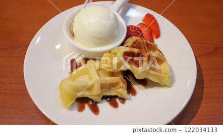 Waffle with vanilla ice cream topping and strawberry slice with chocolate sauce dessert served on white plate. 122034113