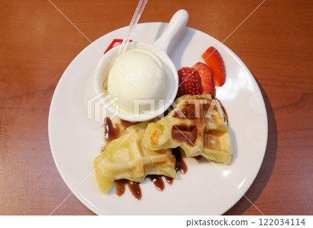 Waffle with vanilla ice cream topping and strawberry slice with chocolate sauce dessert served on white plate. 122034114