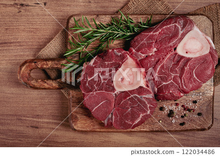 knuckle on the bone, raw meat for ossobuco, on a wooden chopping board, with a sprig of rosemary, and spices, top view, no people, 122034486
