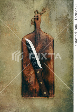 Crafted wooden board with a knife resting on it against a textured background in a kitchen setting Crafted wooden board with a knife resting on it against a textured background in a kitchen setting 122034522