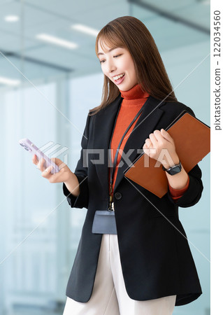 Smiling woman/businesswoman holding a smartphone and a binder Smiling woman/businesswoman holding a smartphone and a binder 122034560