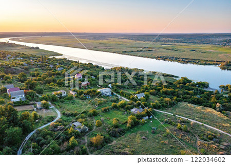 Scenic riverside landscape at sunset reveals serene village tranquility and lush greenery. Aerial photo. 122034602