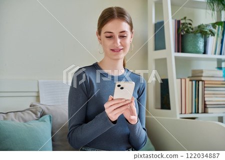 Happy female teenager using smartphone, sitting on couch at home 122034887