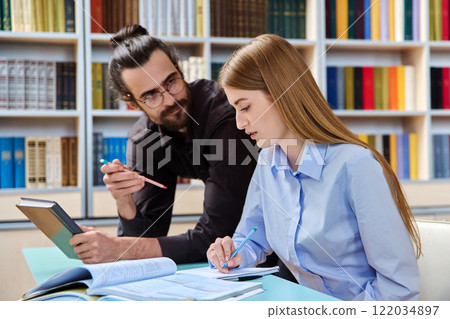 Teenage student girl studying with male teacher inside classroom library Teenage student girl studying with male teacher inside classroom library 122034897