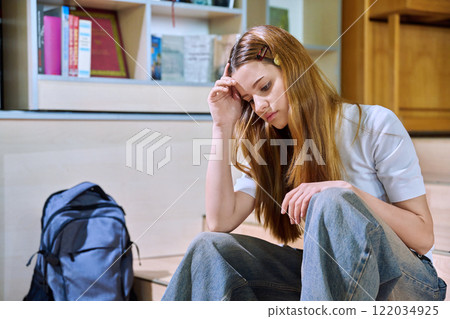 Upset sad teenage girl high school student sitting on floor in library classroom Upset sad teenage girl high school student sitting on floor in library classroom 122034925