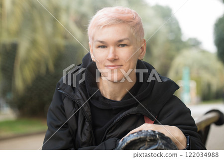 Positive woman with short hair smiling, sitting and looking at camera, outdoors portrait 122034988