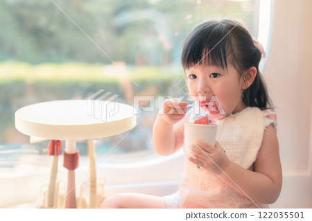 Young Asian Girl Enjoying Delicious Ice Cream Treat in Bright Sunny Indoor Setting 122035501