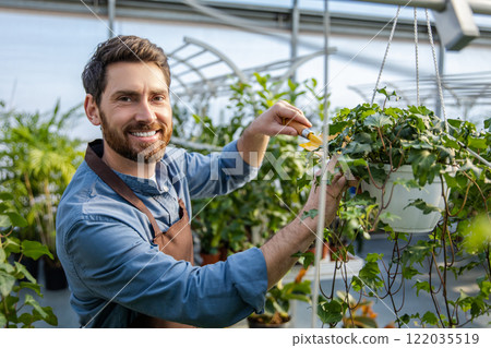 Young bearded man working with plants in a greenhouse Young bearded man working with plants in a greenhouse 122035519