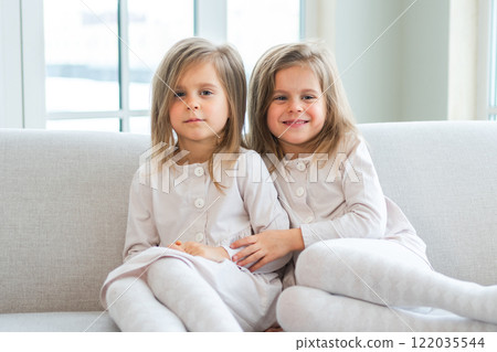 Happy family sisterly love. Two funny little twin sisters girls hugging with love care playing together at home indoors. Happy children lifestyle. Identical twin girls hugs. Girls friendship and youth 122035544
