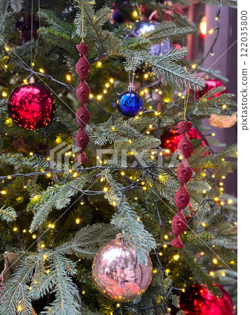 Close-up of a decorated Christmas tree featuring red and blue ornaments with intricate designs. warm fairy lights add a magical glow, highlighting festive details Close-up of a decorated Christmas tree featuring red and blue ornaments with intricate designs. warm fairy lights add a magical glow, highlighting festive details 122035800
