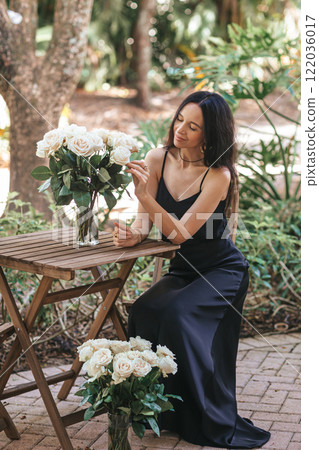 Happy young woman in black dress in outdoor cafe with bouquet of white roses Happy young woman in black dress in outdoor cafe with bouquet of white roses 122036017