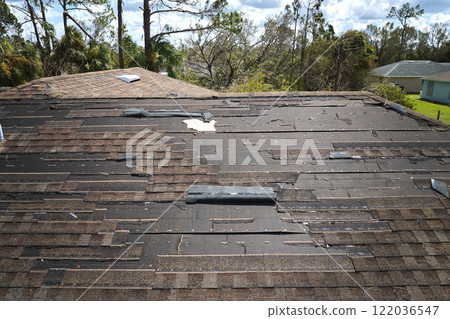 Wind damaged house roof with missing asphalt shingles after hurricane Ian in Florida. Repair of home rooftop concept 122036547