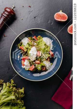 Fresh fig and burrata salad with leafy greens, almonds, and creamy dressing in a rustic blue bowl 122036619