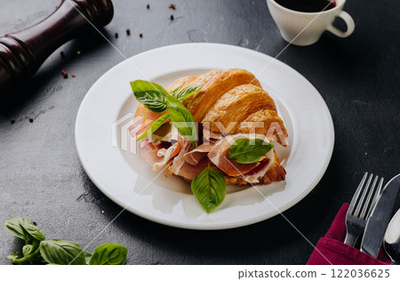 Fresh croissant sandwich with prosciutto and basil served on plate, perfect for a gourmet breakfast 122036625