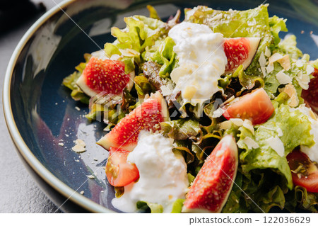 Fresh fig and burrata salad with leafy greens, almonds, and creamy dressing in a rustic blue bowl 122036629
