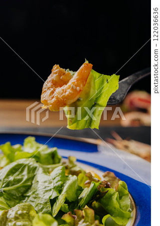Close-up of a fork holding a shrimp and lettuce over a fresh, vibrant salad plate 122036636