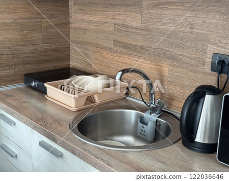Kitchen sink with neatly organized utensils and modern appliances. Sleek design and wooden background highlight functionality and style Kitchen sink with neatly organized utensils and modern appliances. Sleek design and wooden background highlight functionality and style 122036646