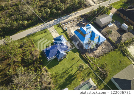 Hurricane Ian damaged house rooftop covered with protective plastic tarp against rain water leaking until replacement of asphalt shingles. Aftermath of natural disaster Hurricane Ian damaged house rooftop covered with protective plastic tarp against rain water leaking until replacement of asphalt shingles. Aftermath of natural disaster 122036781