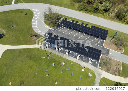 Failing of photovoltaic technology integrated in urban infrastructure. Hurricane wind damage to solar panels installed as shade roof over parking lot for parked electric cars 122036917