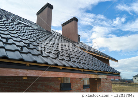 Closeup snow guard for safety in winter on house roof top covered with ceramic shingles. Tiled covering of building Closeup snow guard for safety in winter on house roof top covered with ceramic shingles. Tiled covering of building 122037042