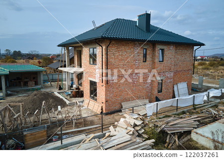 Aerial view of unfinished house with brick walls and wooden roof frame covered with metallic tiles under construction 122037261