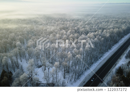 Aerial view of winter landscape with snow covered woods and black asphalt forest road on cold wintry day 122037272
