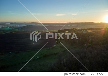 Aerial view of woodland with fresh green trees and agricultural arable fields in early spring at sunset 122037273