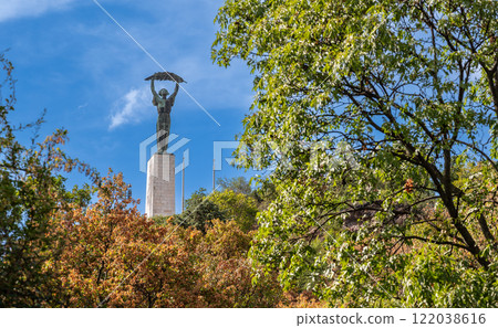 Budapest,Hungary,August 29,2022. The Statue of Liberty dominates the city from the top of the hill, it is an iconic symbol of the capital. On a beautiful summer day the treetops frame the pedestal. 122038616