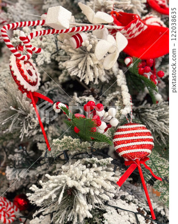 Close-up of a snow-dusted Christmas tree decorated with striped red and white ornaments. Baubles and candy canes and ribbons highlight the festive holiday atmosphere Close-up of a snow-dusted Christmas tree decorated with striped red and white ornaments. Baubles and candy canes and ribbons highlight the festive holiday atmosphere 122038635