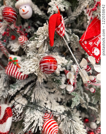 Close-up of a snow-dusted Christmas tree decorated with striped red and white ornaments. Baubles and candy canes and ribbons highlight the festive holiday atmosphere 122038642